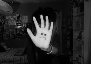 Ung kvinne står på et jenteværelse og holder hånden foran ansiktet. På ansiktet er det tegnet et surt fjes.